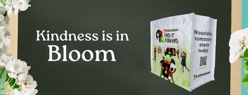 Chalkboard with "Kindness is in Bloom" text and a reusable grocery bag featuring diverse people and "Nourishing tomorrow starts today" message. Surrounding blossoms.