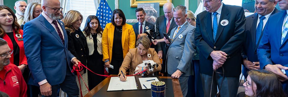 A group of people standing around a table as one person signs a document.